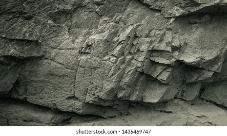 Old Aged Shabby Cliff Face And Divided By Huge Cracks And Layers. Coarse, Rough Gray Stone Or Rock Texture Of Mountains, Background And Copy Space For Text On Theme Geology And Mountaineering.