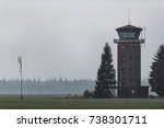 Old air traffic tower in meadow with pine trees.