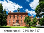 Old Albany Academy Building in Albany, United States, shows red sandstone walls, arched windows and a green cupola rising behind the Joseph Henry statue on a clear summer day
