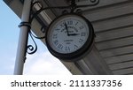 An old analog circular clock inscribed "London Paddington 1854" hangs under a canopy against a blue sky and white clouds, reminiscent of Miss Marple films and old-time England