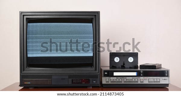 Old analog TV with noise on the\
screen and VCR. Old black TV with VCR on wallpaper background.\
