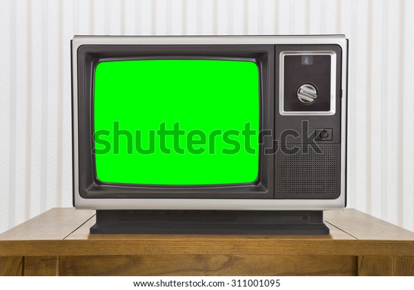 Old analogue portable television on table with\
green screen.