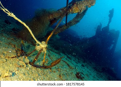 Old Anchor Laying On The Sea Bottom With Some Shipwreck Remnants In The Background 