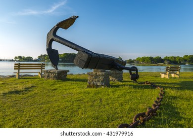 An old anchor sits idly by the coast of New England on a bright blue morning.  