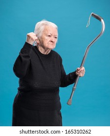 Old angry woman threatening with a cane on a blue background