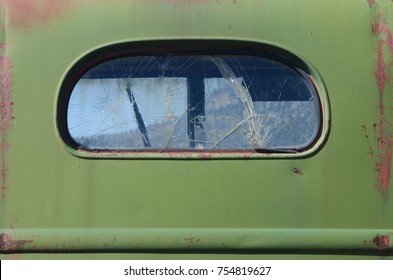 An Old Antique Truck Rusts Slowly In A Mountain Field, With A Rear Window That Is Cracked Into Hundreds Of Pieces Of Glass.  Its View Through The Front Window Is Of The Mountains Beyond.  