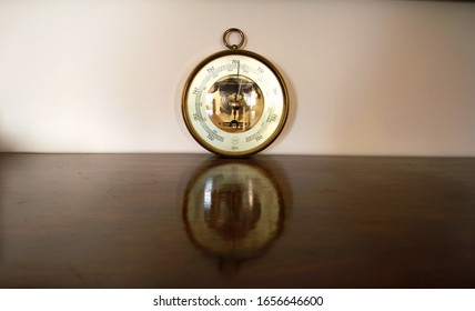 An old antique vintage brass barometer hanging, on wooden table. There is a beautiful reflection   - Powered by Shutterstock