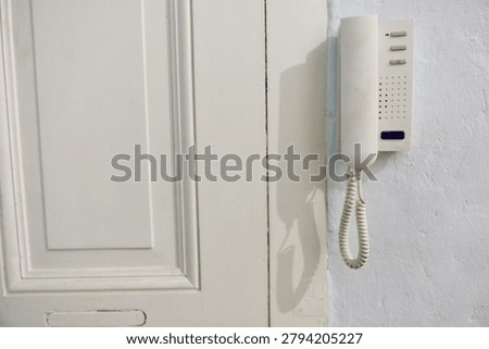 An old apartment intercom system is mounted on a white wall next to a classic white door in a building in Berlin Prenzlauer Berg, showcasing the pre renovation state of the property.