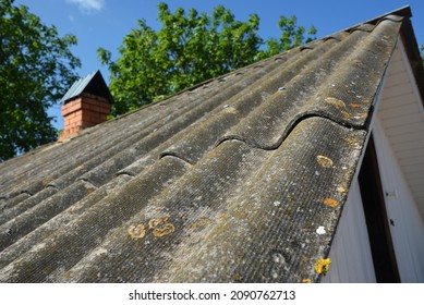 An old asbestos pitched roof. A close-up of an old asbestos roof tiles covered with moss and lichen. - Shutterstock ID 2090762713