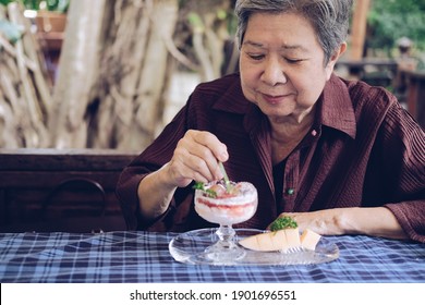 Old Asian Elderly Senior Elder Woman Eating Strawberry Panna Cotta Dessert At Restaurant. Mature Retirement Lifestyle