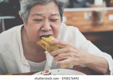 Old Asian Elderly Senior Elder Woman Eating Vegan Wrap Stuffed With Quinoa, Black Bean, Mango, Cashew Nut, Bell Pepper