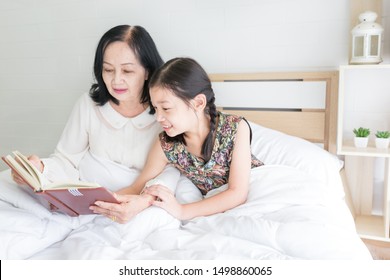 Old Asian Female And Asian Children Reading Book On White Bed, Old Asian Woman Talk About Tale To Her Daughter, Retirement Happiness, Elderly Activity