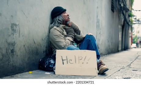 An Old Asian Man, A Homeless Man, Dressed In Shambles With A Sign For Help, Hoping Beside Him, Watches Passers-by, Hoping Someone Will Help Him Because He Has No Money, Food, No Job.