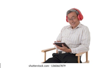 A old Asian man sitting on a chair enjoy using tablet listening to music wearing red headphone on isolated white background. - Powered by Shutterstock