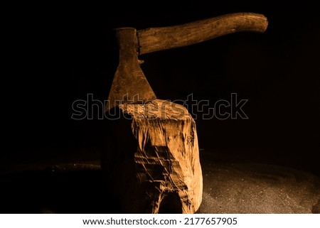 Old ax attached to the tree trunk on horror red foggy background. Scary Halloween theme with maniac killer weapon. Empty space. Selective focus