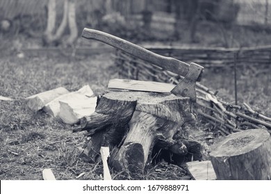 Old axe in tree stump on cottage glade at summer day. Black and white retro toned image.
