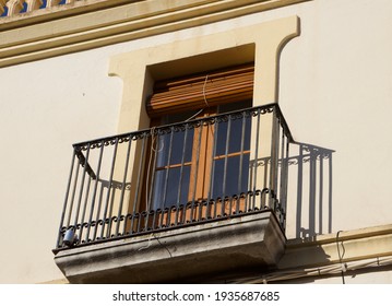 An old balcony in full morning sunshine. A wooden shutter is rolled up ready for the day to commence. The railings are in the sun and their pattern gives extra body to the rustic, charming town image.