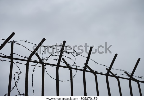 Old barbed wire fence in silhouette fencing an\
industrial site