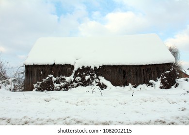 Old barn completely covered and surrounded with snow during heavy snowfall with cloudy sky in background