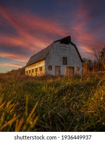Old Barn in the middle of the country with a beautiful pink and red sunset behind it. Taken in the middle of a field.