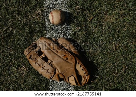 Old baseball glove with ball on foul line of outfield grass with copy space on sports background.