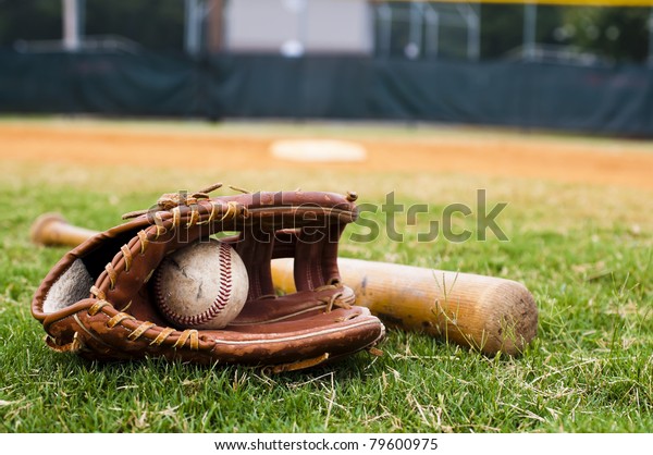 Old baseball, glove, and bat on field with\
base and outfield in\
background.