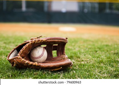 Old baseball and glove on field with base and outfield in background.