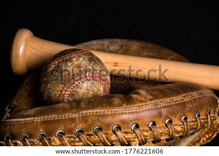 Old baseball, stained and wonrn out, and old style catchers mitt joined by a brand new baseball bat.