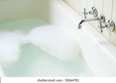 Old Bath Tube With Bubbles, Water And Hot And Cold Tap