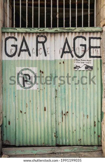 Old battered\
garage doors. Signs warning about prohibition of parking and\
evacuation of parked cars. Gzira,\
Malta.