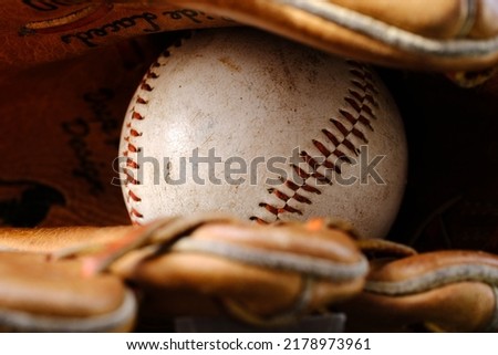 An old beat up baseball sitting in a vintage leather baseball glove