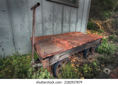 Old beat-up rusted wagon with nails showing sitting in the weeds by an old shed.