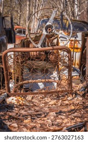 Old bed frames and classic car interior parts with steering wheel scattered in forest scrapyard scene.