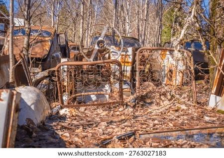 Old bed frames and classic car interior parts with steering wheel scattered in forest scrapyard scene.