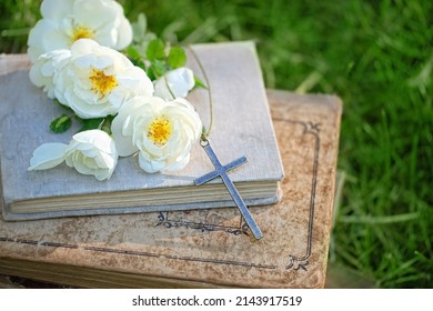 old biblical books, Christian cross and rose flowers in garden, green natural background. symbol of Easter, Orthodox palm Sunday. Christianity, Lent, Faith in God, Church holiday concept