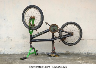 An old bicycle of a decayed boy was placed upside down next to a cement wall.
