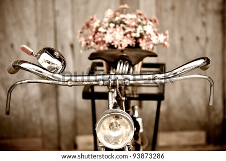 Old bicycle and flowers blur in background process in vintage old style film. Classic design bike with wood wall out focus behind.