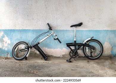 Old bicycle with a frame broken in half stands against a battered concrete wall outdoors. Two halves of the bike are standing against a shabby wall.