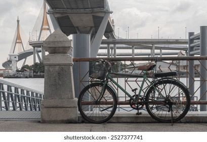 An old bicycle parked on the side in the ferry pier with Bhumibol suspension bridge cross over Chao Phraya River in the background. Space for text, Selective focus. - Powered by Shutterstock