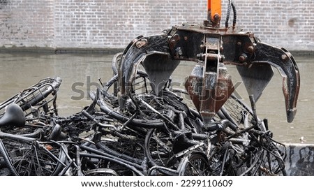 Old bicycles being pulled from a canal and loaded onto a barge by a mechanical claw in Amsterdam, Netherlands.