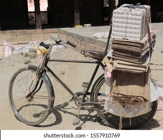 Old bike with cardboard tied onto the back to recycle. Dusty street.
