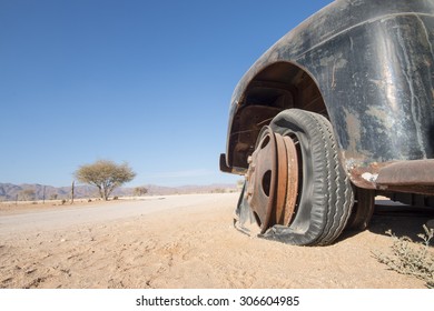 Old, Black Car With A Flat Tire In The Desert, Concept For Offroad Sport Or Traveling And Adventure, Namibia, Africa