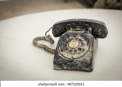 Old Black Rotary Phone Covered In Burning Man Nevada USA Desert Sand And Dust On A Light White Table.