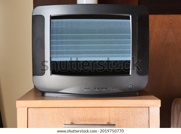 An old\
black TV with noise on the screen sits on the bedside table in the\
apartment. Vintage TVs 1980s 1990s 2000s.\
