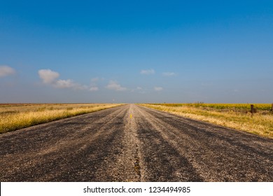 Old Black Worn Country Road Against Blue Sky In Rural Texas, USA