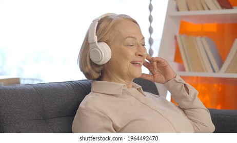 The Old Blond Woman, Having Fun Listening To Music From The Headphones, Leans Her Head Back And Keeps The Rhythm. The Portrait Of Keeping Rhythm With Music. Front Side Angle.