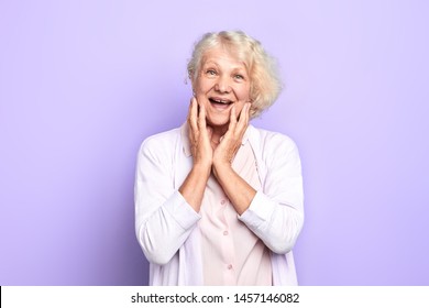 Old Blonde Girl Touching Face With Palms, Expresses Happiness And Joy. Isolated Blue Background. Studio Shot Woman Has Heard That She Would Get Big Pension