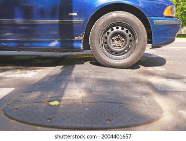 Old Blue Car Runs Over A Speed Bump, Speed Control On The Street. Black Rubber Speed Bump. Car Wheel. Sleeping Policeman Closeup, Speed Reduce