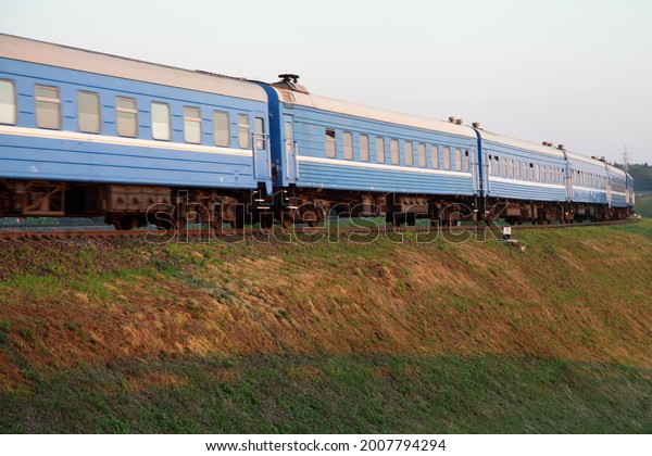 Old blue passenger train motion bottom up side\
view at sunny summer\
evening