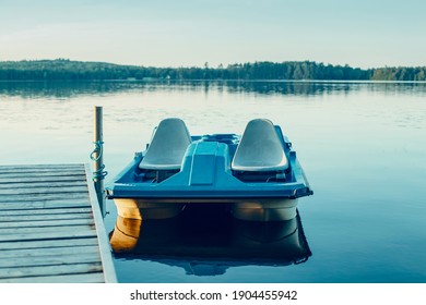 Old blue pedal boat tied to wooden dock pier. Beautiful idyllic calm serene landscape sunset summer view at Canadian Ontario lake in Muskoka. Travel Canadian local destination water nature place. 